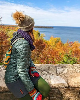 A woman sitting on a wall looking out at the fall trees