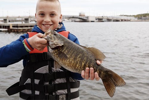 A young kid holding up a fish he caught.