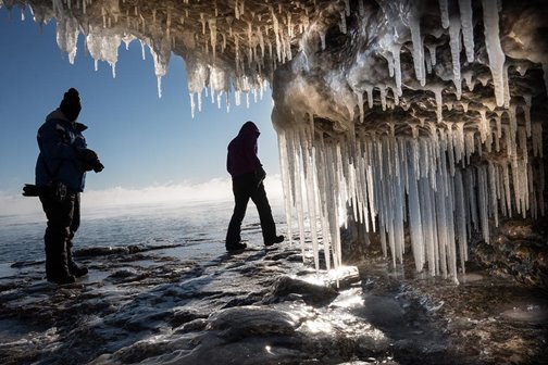 People hiking near an ice cave at the lakefront.