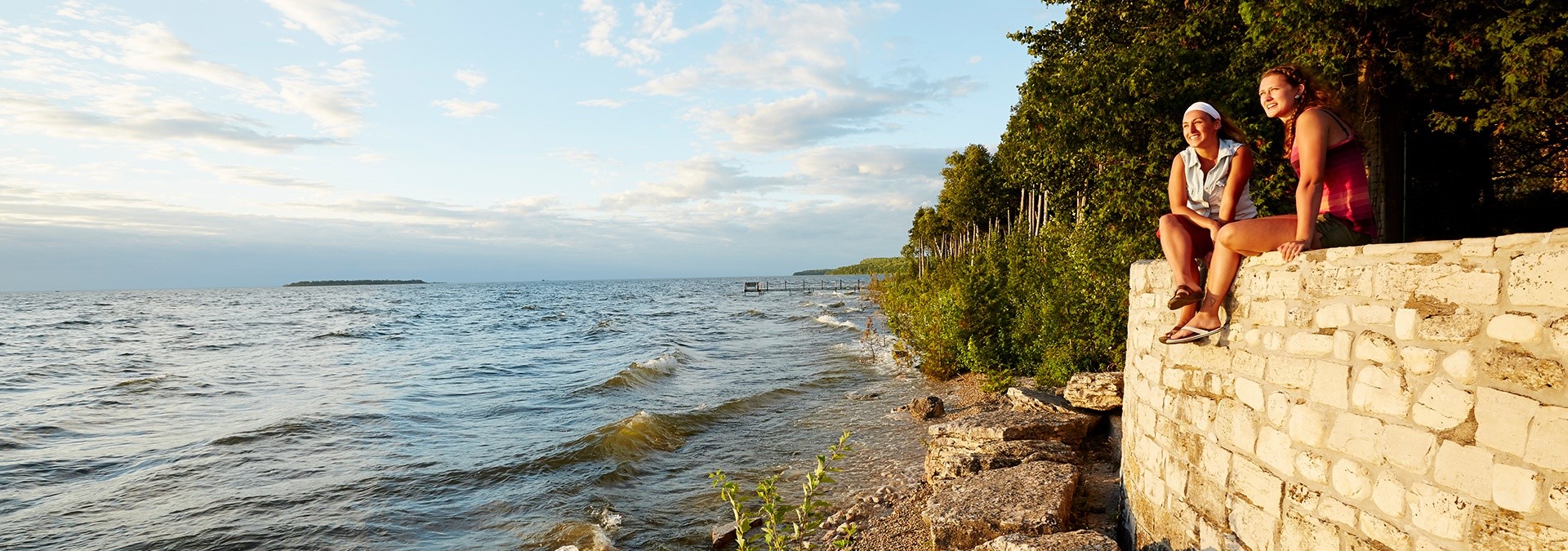 Two people sitting on a stone wall looking out at the lake