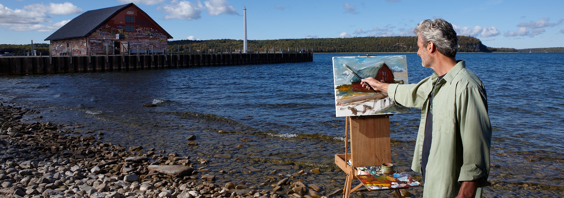 Man painting a barn at the lakefront.