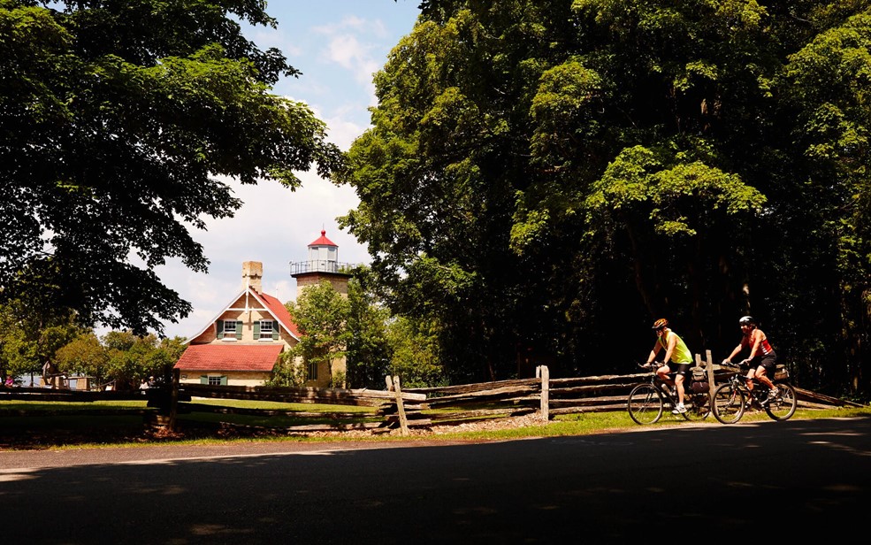 Two people biking with a lighthouse in the background.