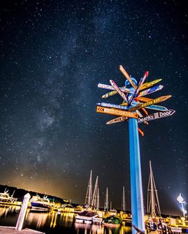 A signpost with signs pointing in all directions lit up at night.