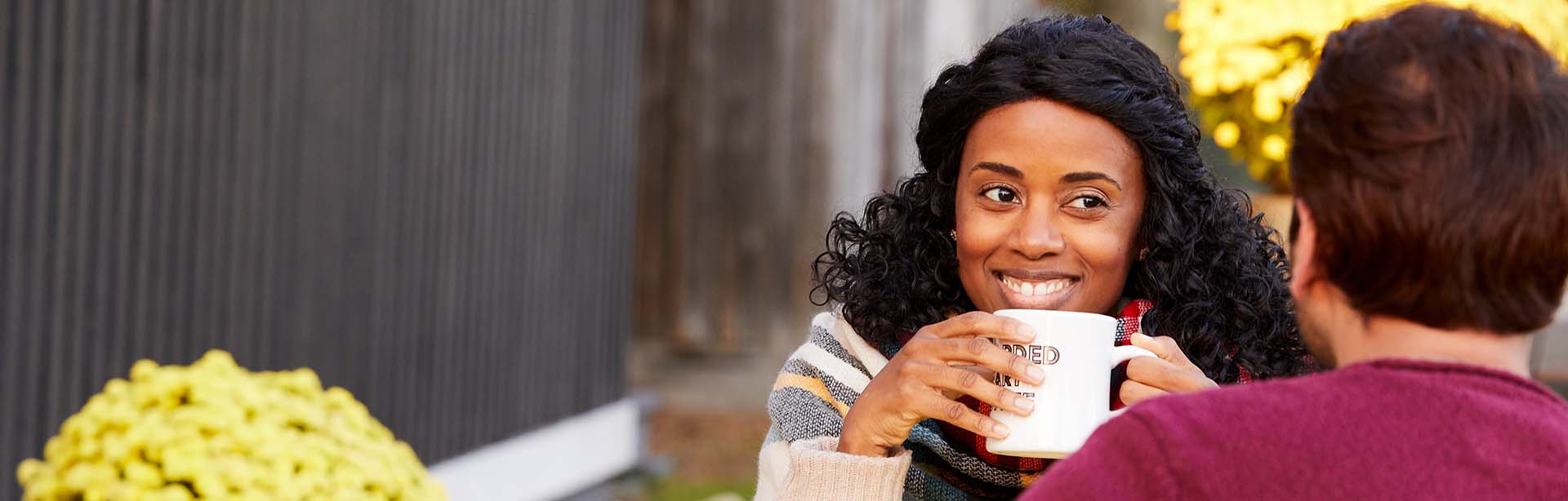 A couple enjoying coffee and the woman is holding a coffee mug and smiling