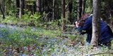 A woman in the woods taking a picture of flowers.