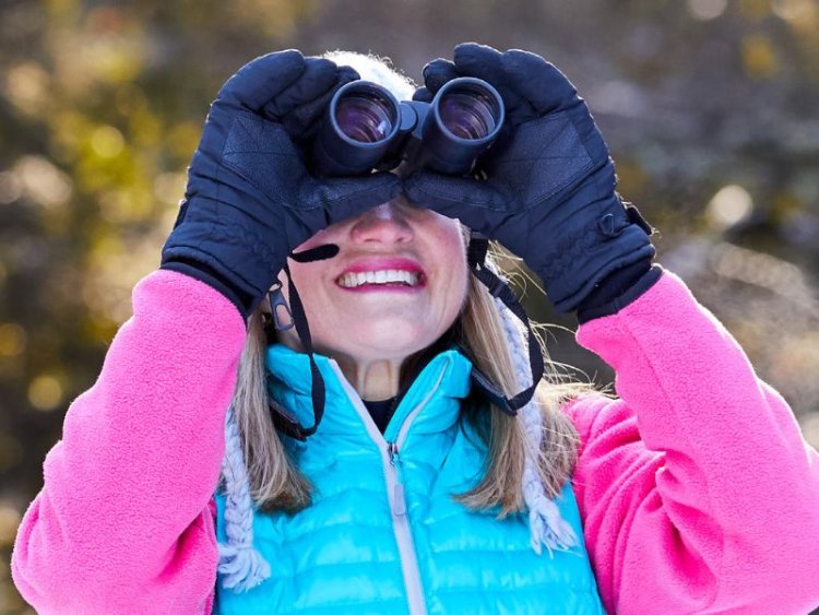 A person in vibrant winter gear holding binoculars while birding.
