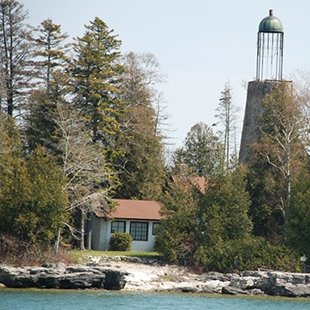 An old lighthouse surrounded by trees at the lakeshore.