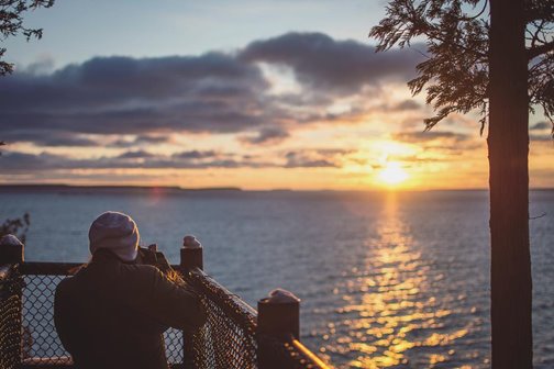 A person taking a picture of the sunsetting over the lake