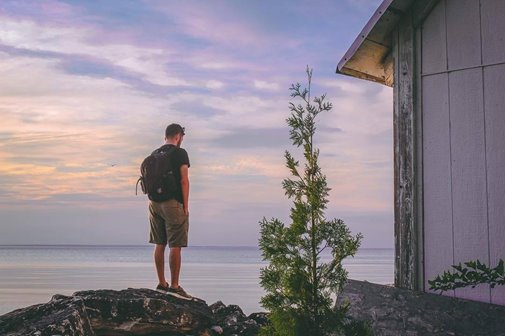 A man with a backpack standing on a rock looking out at the lake