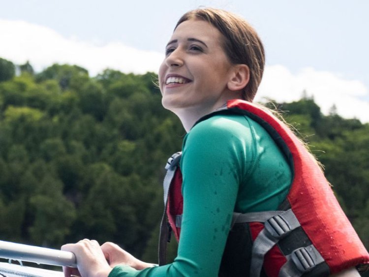 Woman holding onto a boat wearing a life vest looking excited about their adventure.