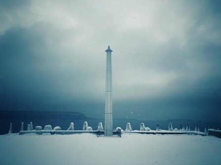 A lighthouse at the edge of the lake in the snow.