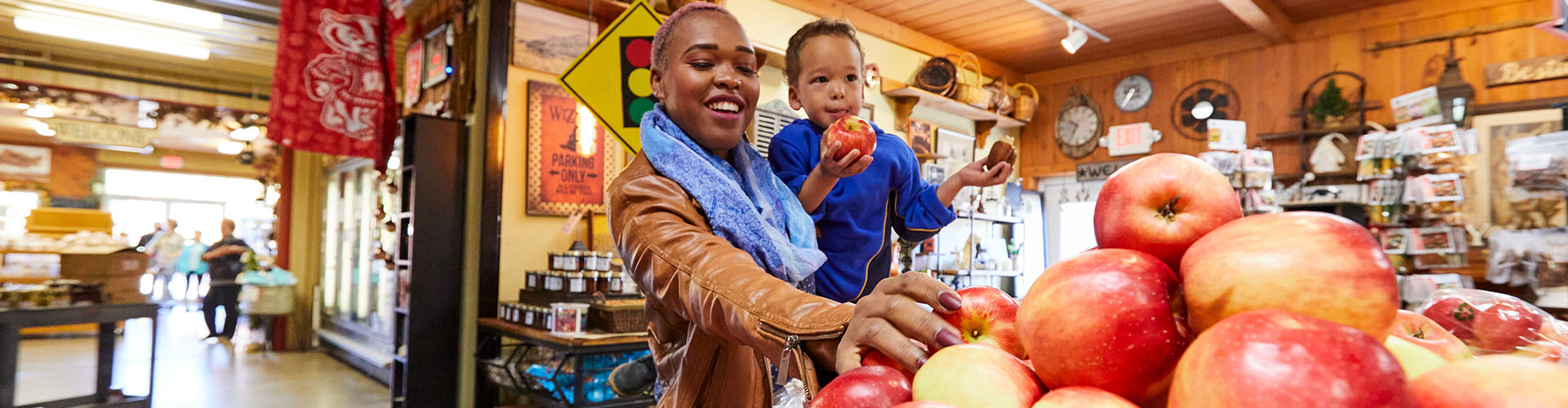 A woman holding her child while picking an apple at a market