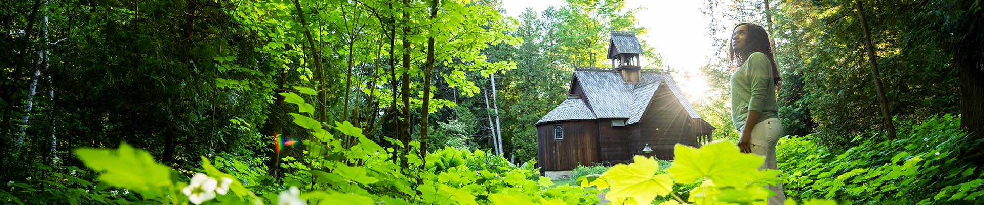 A woman immersed in nature and sunlight near a wooden building.