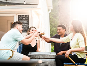 Friends cheering with wine glasses around a fire pit.