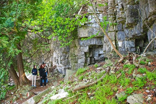 People walking at the base of a stone cliff.